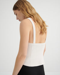 A woman shown from the back wearing a white structured strap top and a black skirt, photographed against a clean light gray studio background.