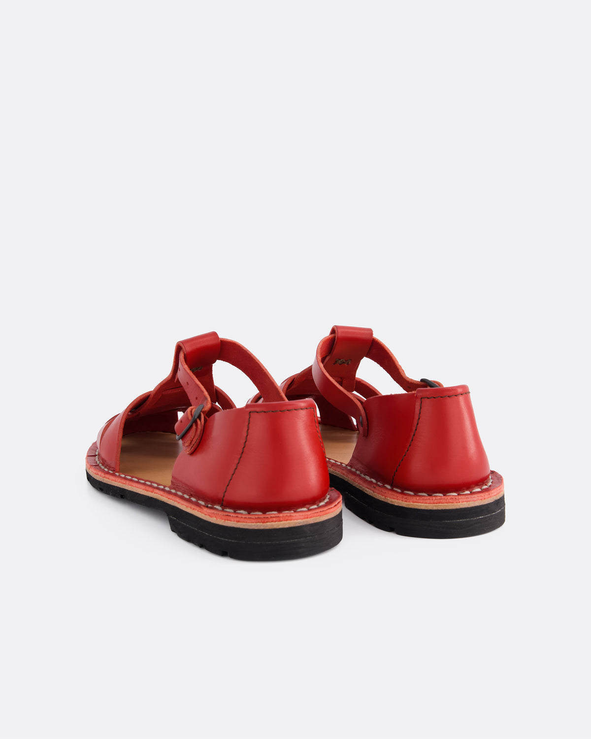 A pair of red leather flat sandals shown from the back on a light gray background.