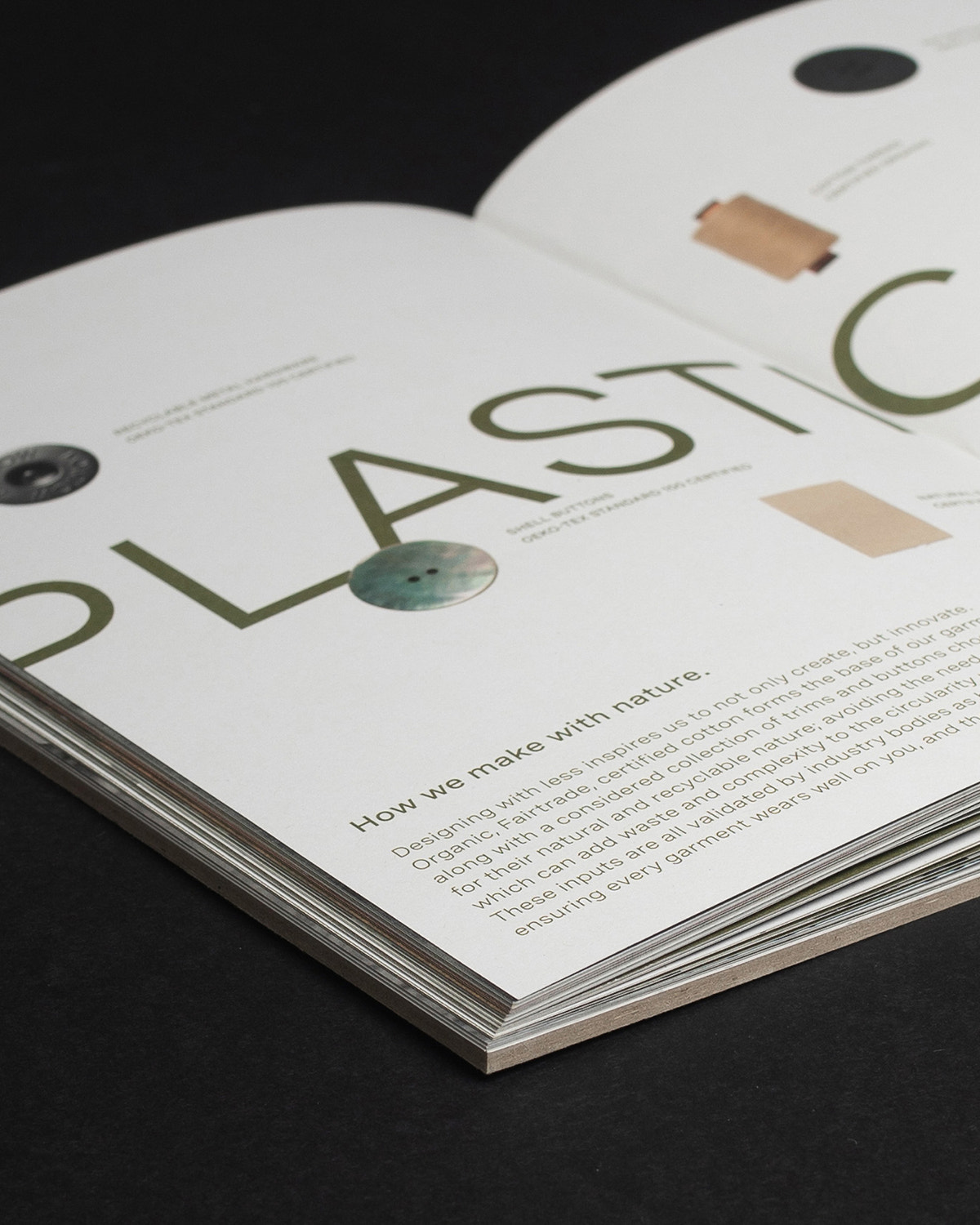 An open printed magazine or booklet on a dark surface, showing a page with large green text reading 'PLASTIC' and smaller text about making with nature, alongside small material samples and circular cutouts.