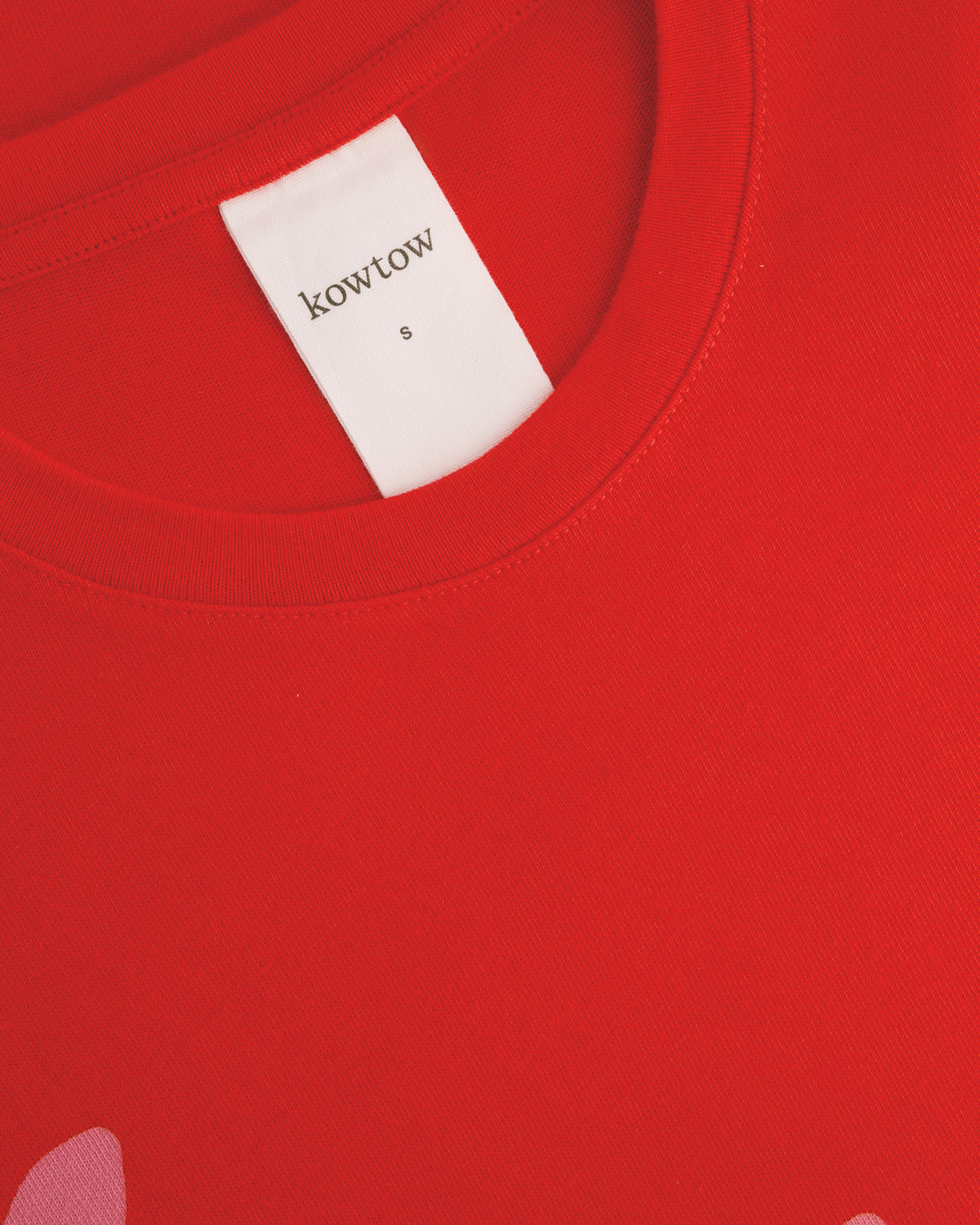Close-up of a bright red crewneck sweatshirt showing a white neck label with the brand name 'kowtow' and a small size 'S' printed on it.