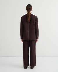 A model viewed from the back wearing a dark brown tailored jacket and matching wide-leg trousers against a plain light gray studio background.