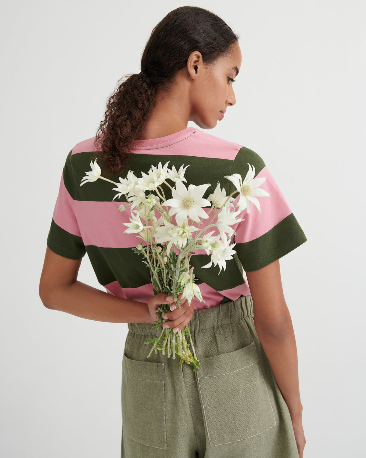 Woman holding flowers wearing a striped shirt with floral patterns on a plain background
