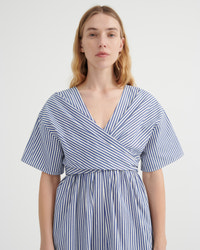 A woman modeling a blue and white vertically striped wrap dress with short flutter sleeves and a V-neckline, photographed against a plain light gray studio background.