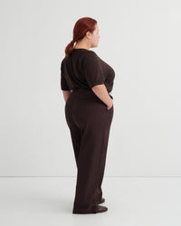 A woman with red hair tied back is shown from the back wearing a dark brown short-sleeve top and matching dark brown wide-leg trousers.