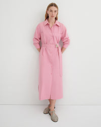 A woman modeling a light pink long-sleeve shirt dress with a matching tie belt, standing against a plain white studio background.