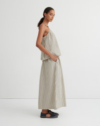 A model wearing a matching beige and white striped two-piece set consisting of a sleeveless wrap-style top and wide-leg trousers, paired with dark flat shoes, set against a plain white studio background.