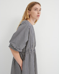 A woman wearing a loose-fitting, short-sleeved dress with vertical gray and white stripes, shown from a side profile against a plain light gray background.
