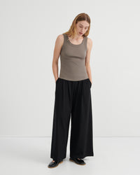 A woman modeling a sleeveless taupe ribbed tank top and black wide-leg trousers.