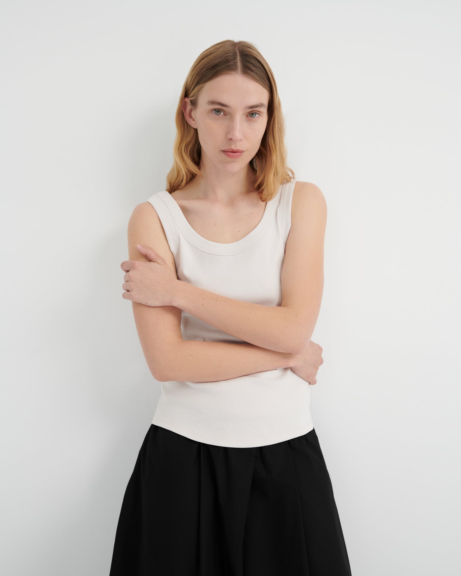 A woman with blonde hair wearing a white ribbed scoop-neck tank top and a black skirt.