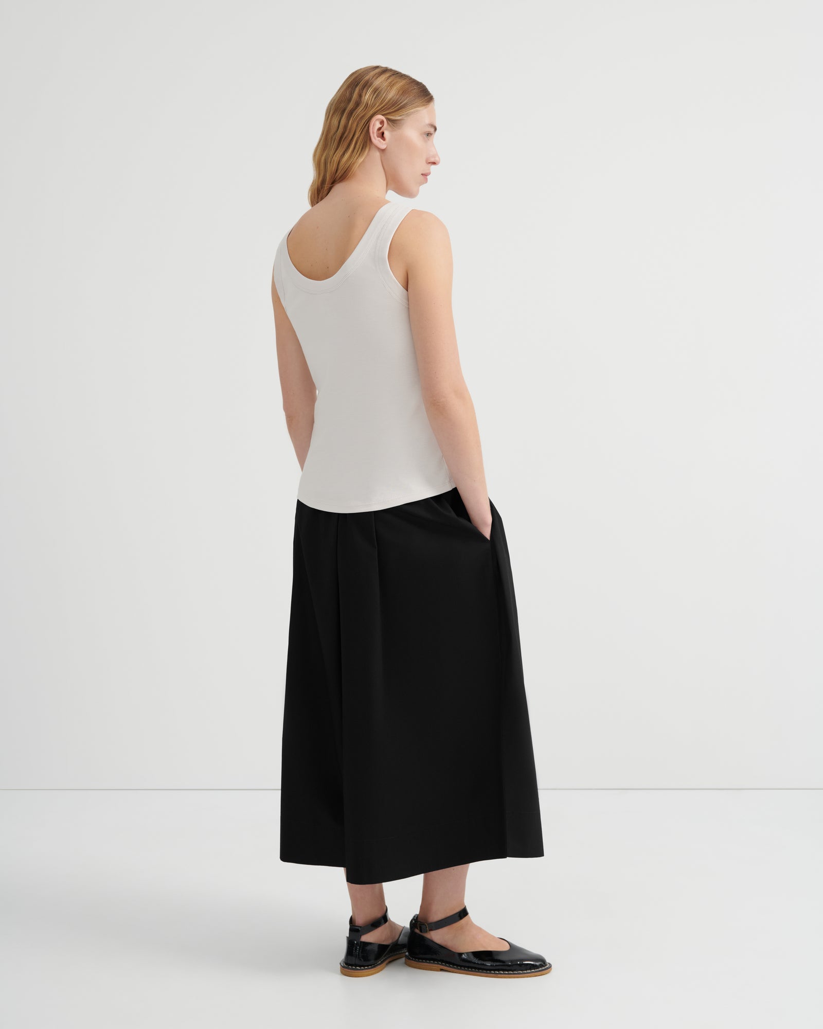 A woman shown from the back wearing a off-white ribbed tank top and a black midi skirt, paired with black flat sandals.