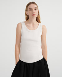 A woman modeling a fitted sleeveless scoop-neck tank top in off-white, paired with a black skirt.