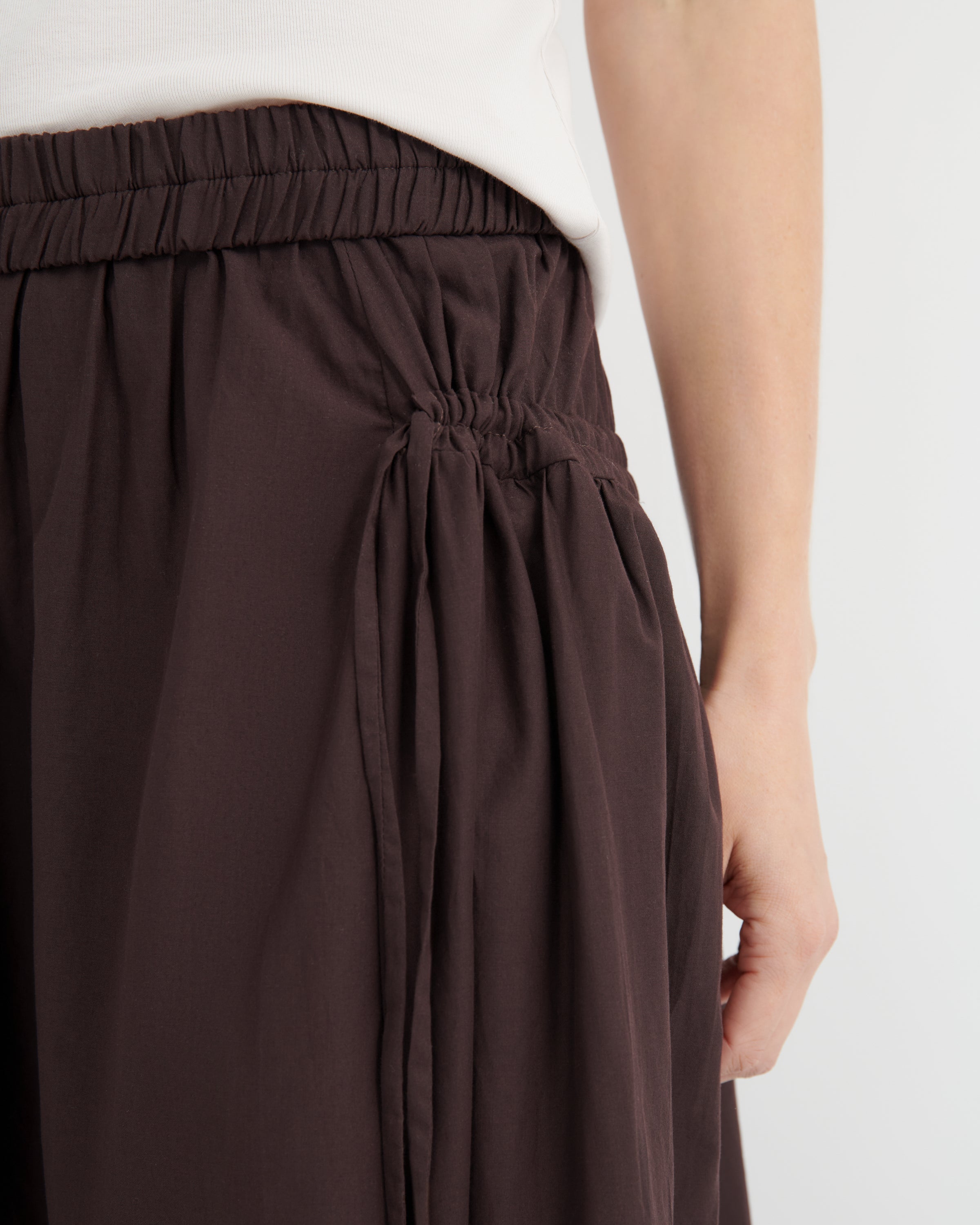 Close-up of a person wearing dark brown wide-leg gathered skirt with an elastic waistband, paired with a white top.