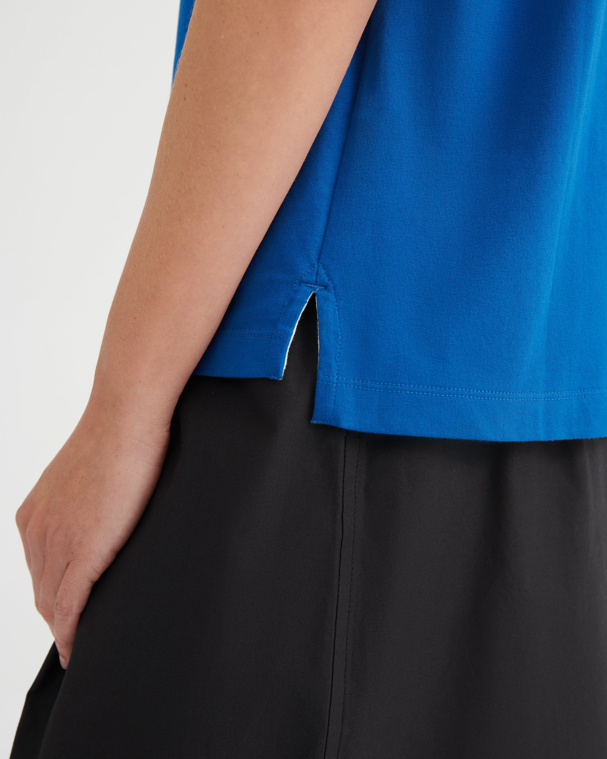 Close-up of a person wearing a bright blue sleeveless top with a side slit and black bottoms against a plain light background.