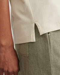 Close-up of a person wearing a light beige short-sleeve top and an olive green textured skirt or trousers, showing the hem detail and fabric texture.