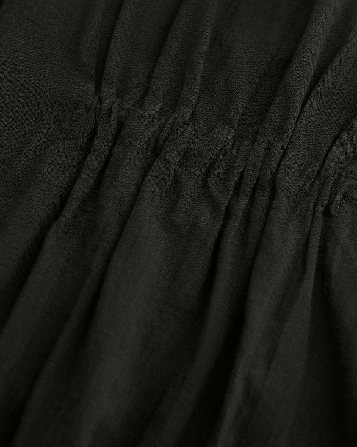 Close-up of dark olive green fabric with a gathered waist seam and visible stitching.
