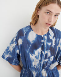 A close-up of a model wearing a blue and white tie-dye short-sleeve top with a buttoned neckline and gathered waist.