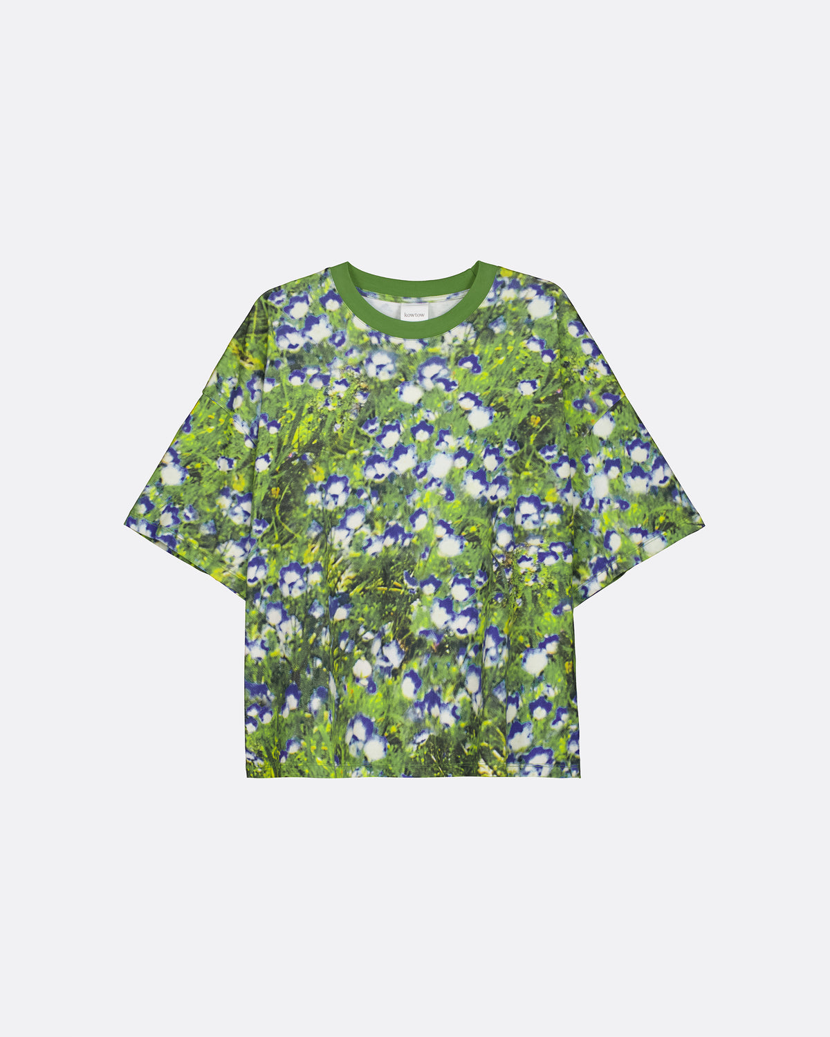 A short-sleeve crewneck t-shirt featuring an all-over floral print of blue and white flowers on a green background, displayed flat against a light gray studio backdrop.