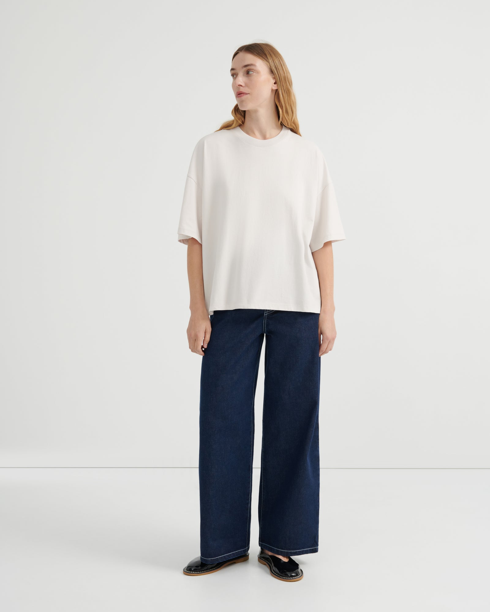 A woman wearing an oversized off-white short-sleeve top, dark blue wide-leg jeans, and black loafers.