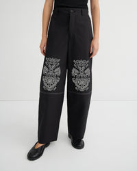 Black pants with white floral embroidery on a white background