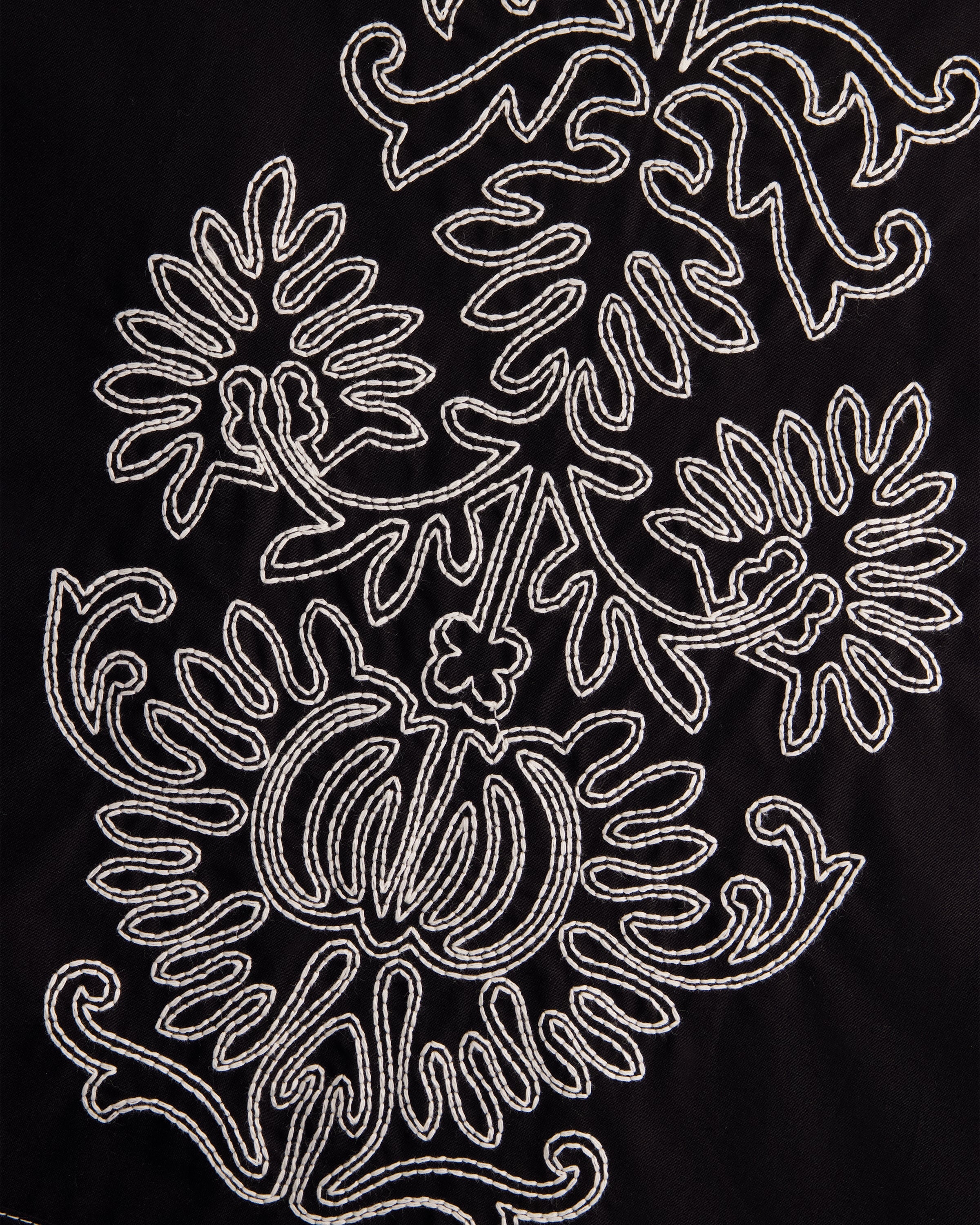 Close-up of a black fabric surface with an ornate white embroidered floral and scroll pattern.