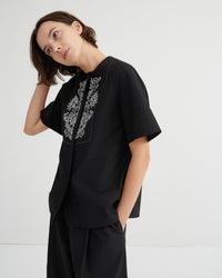Person wearing a black outfit with white embroidery on a plain background