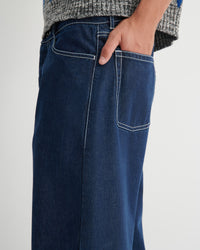 Close-up of a person wearing dark blue denim jeans with white contrast stitching and a gray knit sweater.
