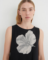 A woman wearing a sleeveless black top with a large gray watercolor-style hibiscus flower graphic on the front, photographed against a plain light gray background.