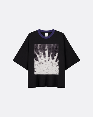 A black short-sleeve t-shirt with a blue ribbed crew neck and a square graphic print on the front featuring a black and white abstract design with circular details, displayed on a light gray background.