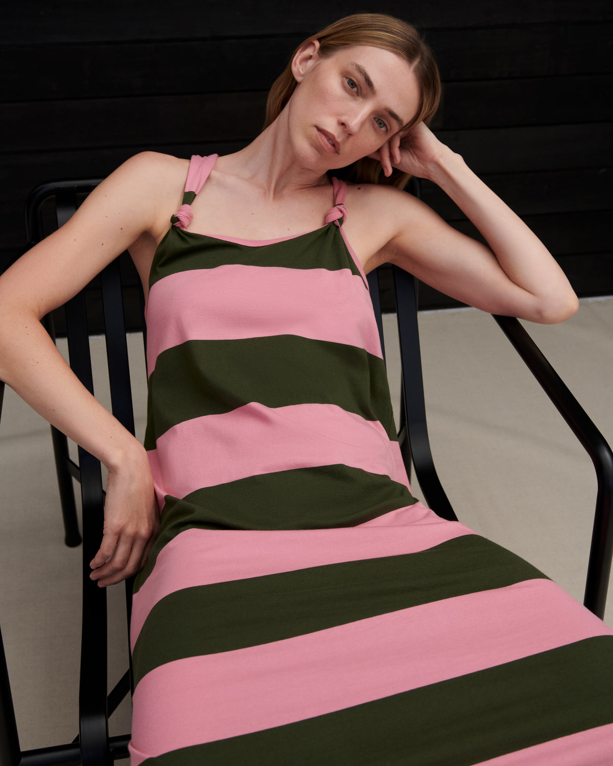 Woman wearing a pink and green striped dress sitting on a chair.