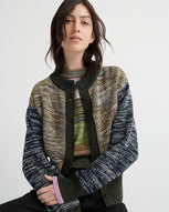 A women sits in front of a light grey background wearing a patchwork cardigan over a patchwork vest.
