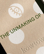 A close-up of a kraft paper package or card with white circular cutouts and green text reading 'THE UNMAKING OF' and 'kowtow'.