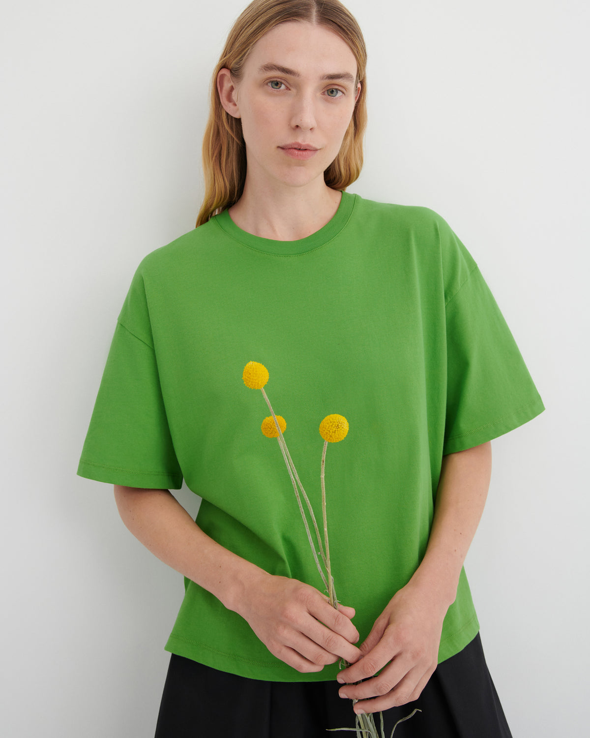 Women wearing a green tee and black trousers holding yellow flowers.