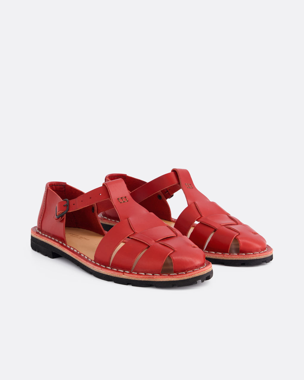 A pair of red leather strappy sandals with a flat sole, displayed on a clean light gray background.