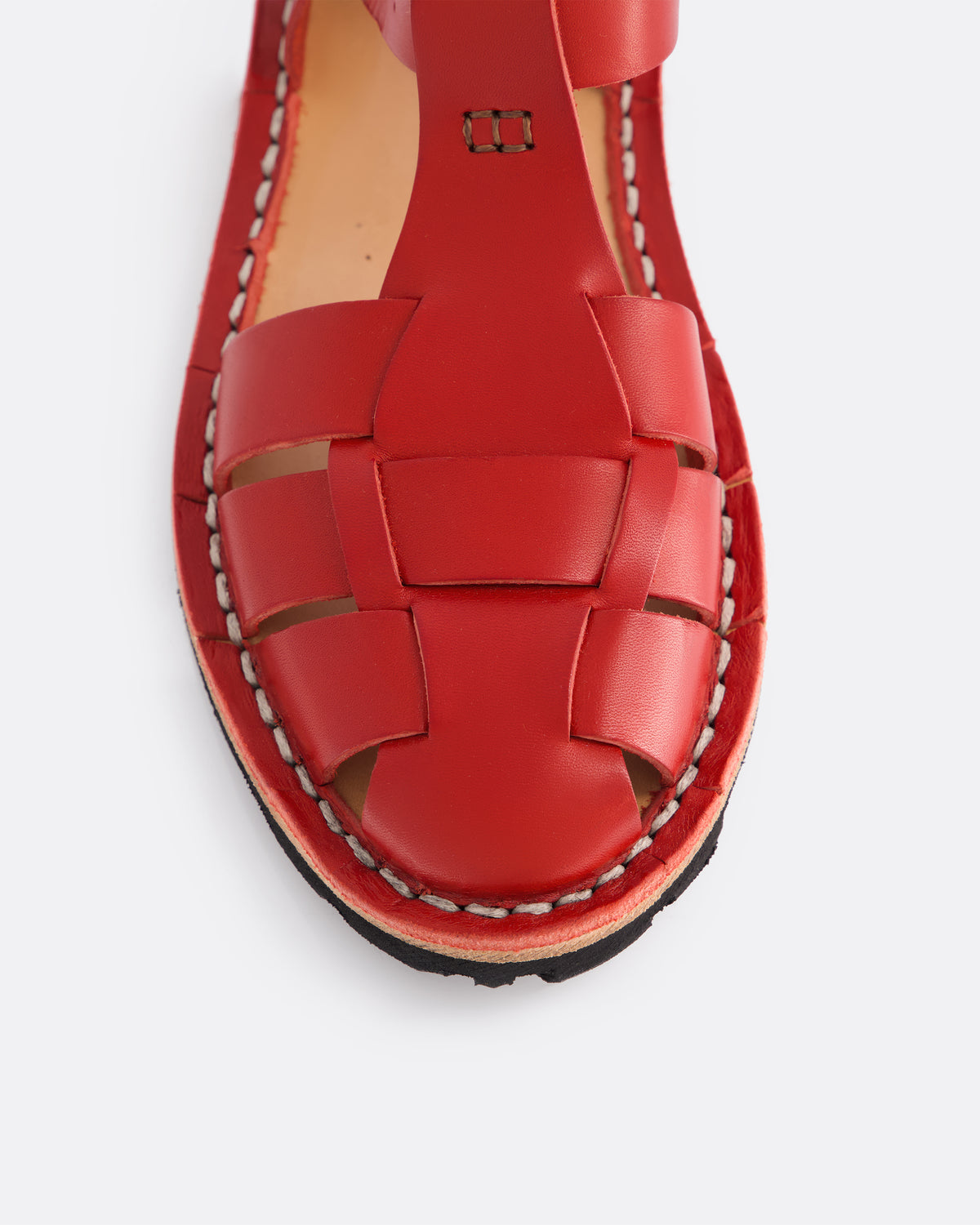 A close-up top-down view of a red leather sandal with a woven strap pattern and contrast stitching, set against a light gray background.