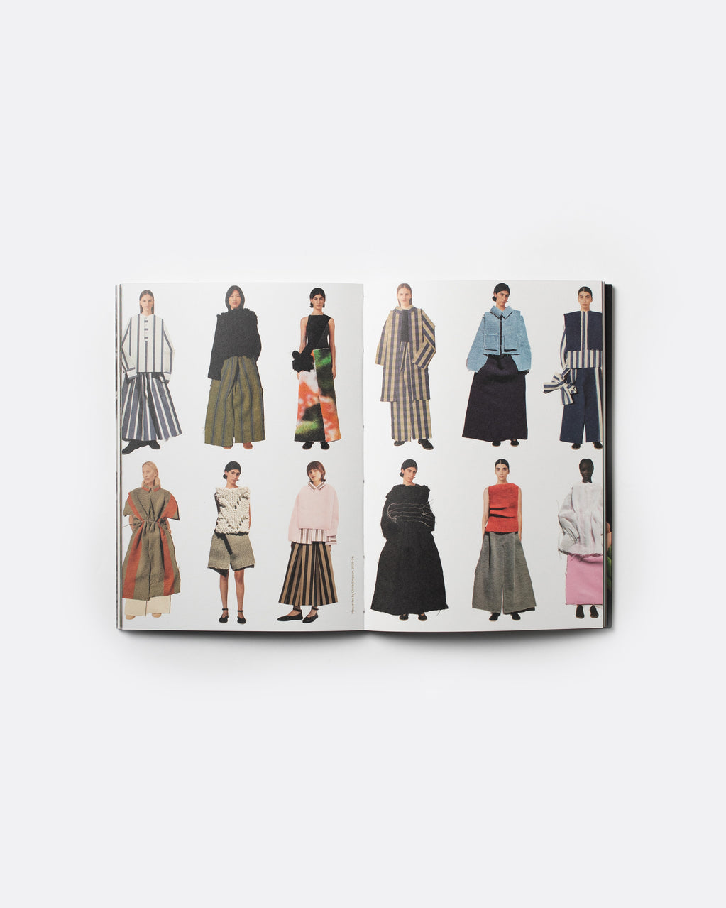 An open fashion magazine or book spread displaying multiple illustrated models wearing different outfits, photographed against a clean white background.