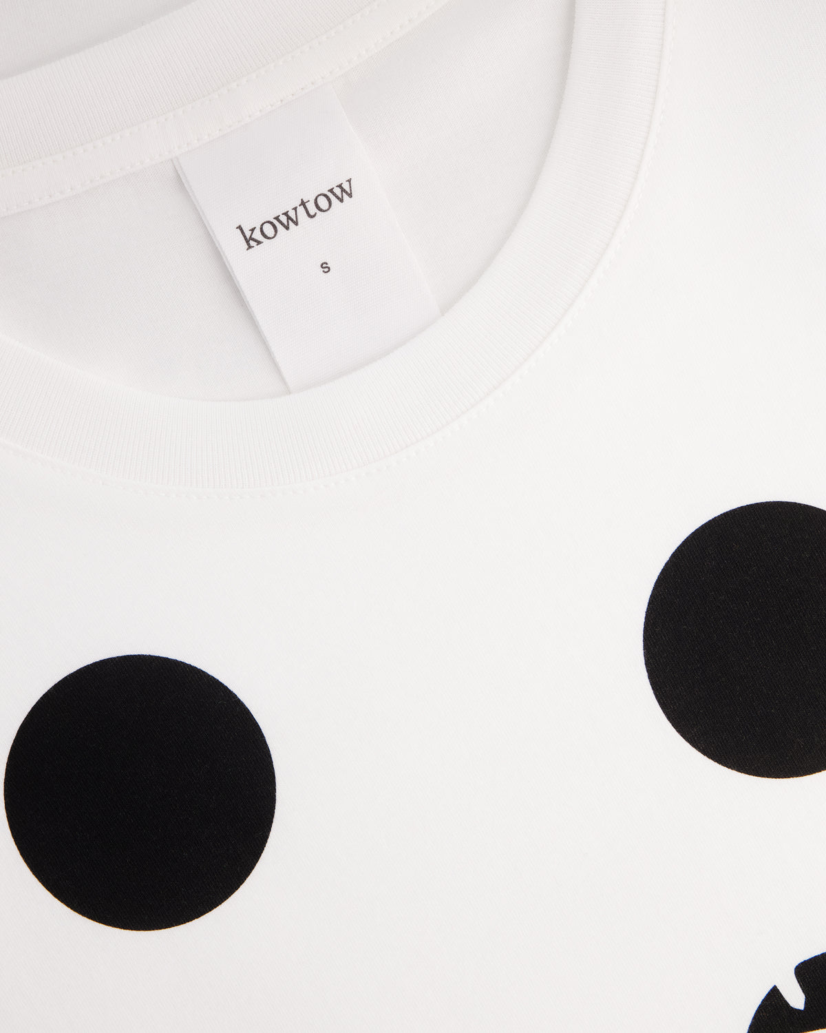 Close-up of a white crewneck t-shirt with black polka dots, showing the inner neck label with the brand name 'kowtow'.