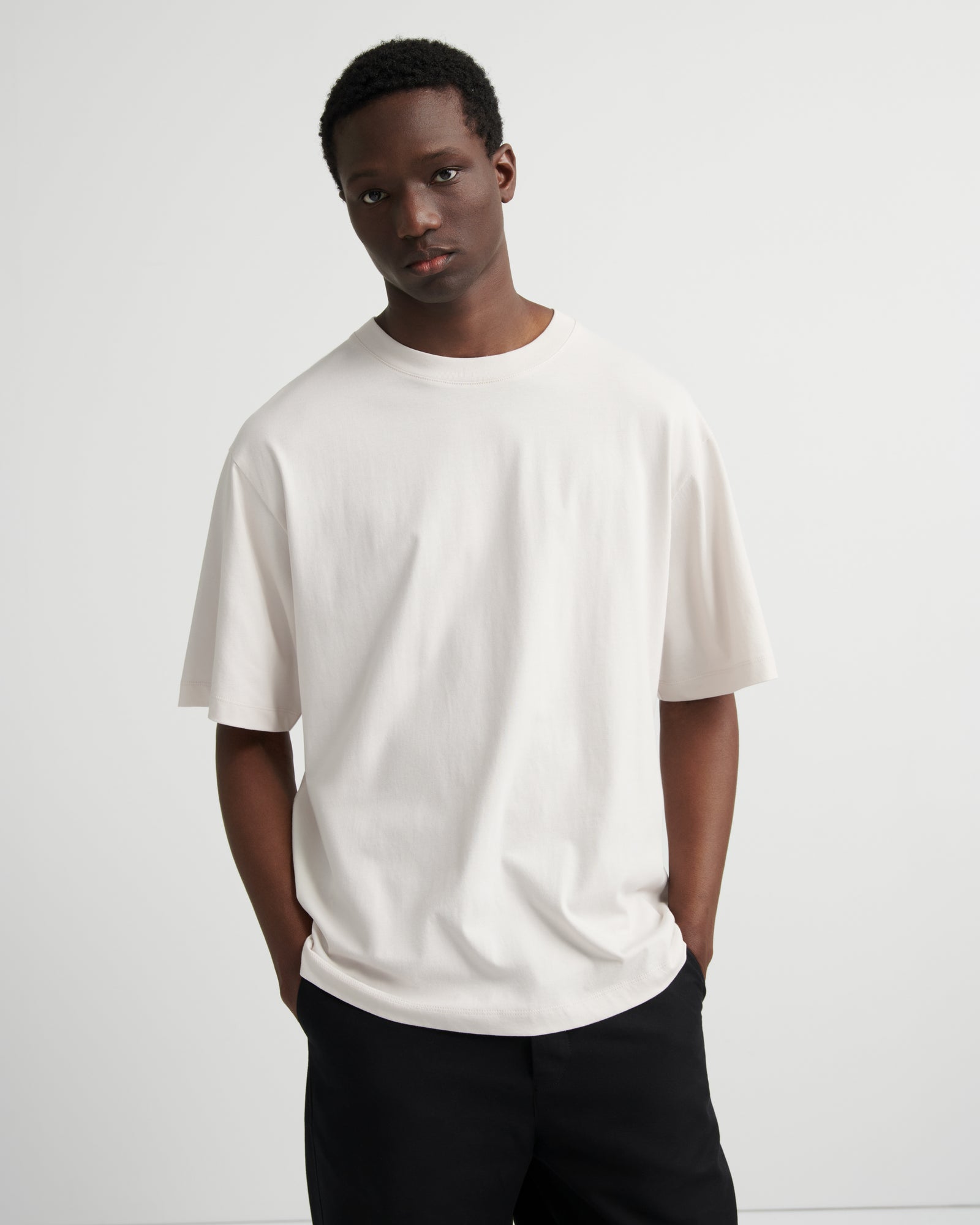 A man wearing an oversized off-white crewneck t-shirt and black pants.