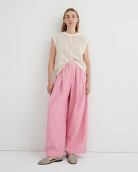 A model stands against a plain white studio background wearing a cream sleeveless knit top, pink wide-leg drawstring pants, and beige flat sandals.