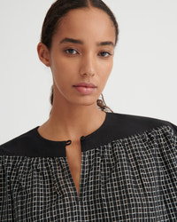 A close-up of a model wearing a black and white checkered top with a solid black collar and button placket, set against a plain light gray background.