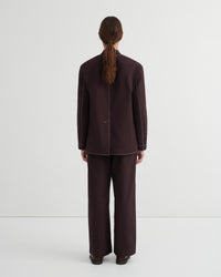 A model viewed from the back wearing a dark brown tailored jacket and matching wide-leg trousers against a plain light gray studio background.