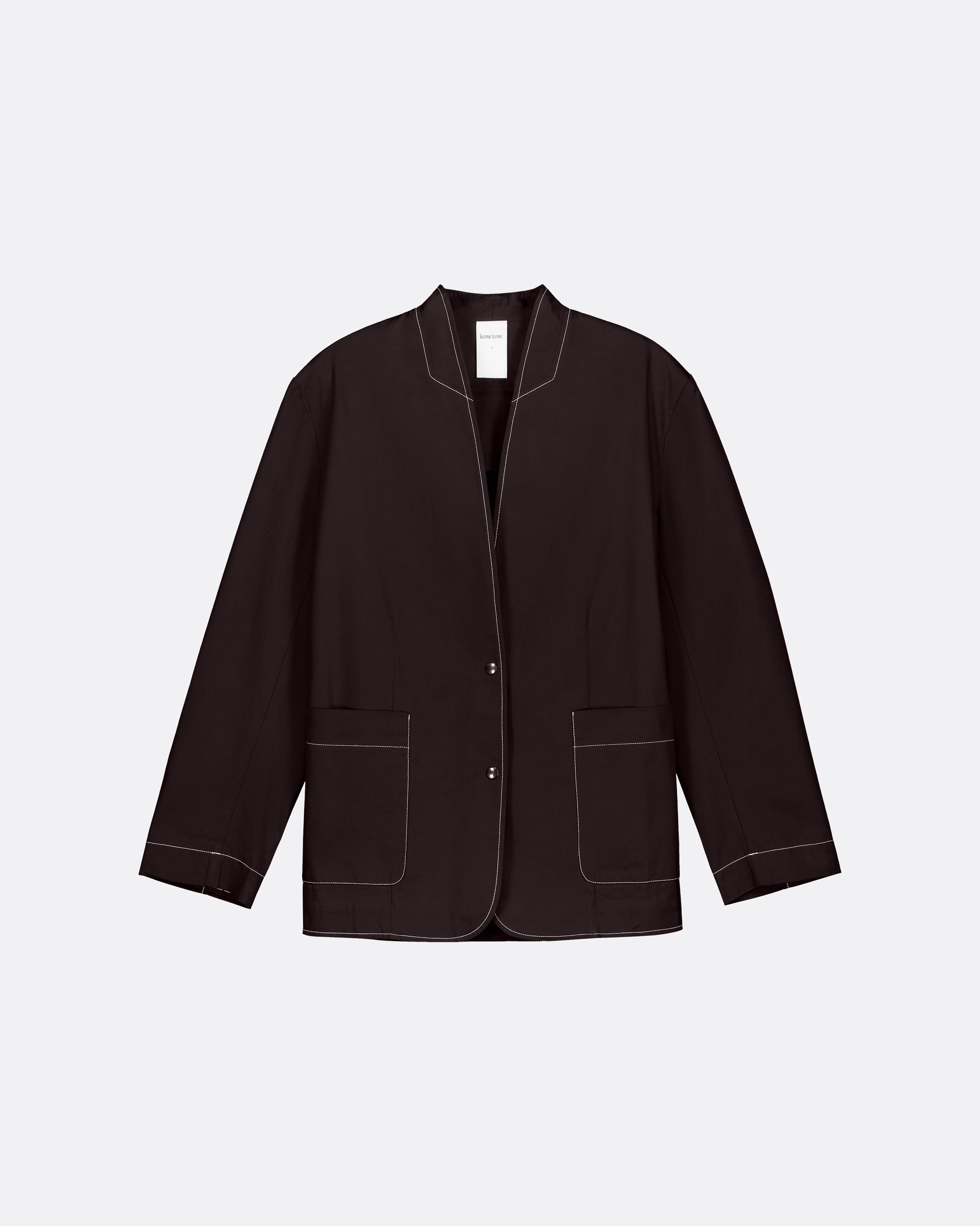 A dark brown blazer with white contrast stitching, featuring a stand collar, button front, and two front patch pockets, displayed on a light gray background.