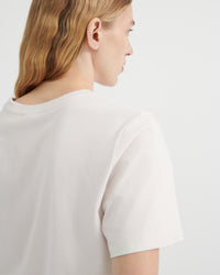 A close-up side profile of a woman wearing an off-white short-sleeve crewneck t-shirt.