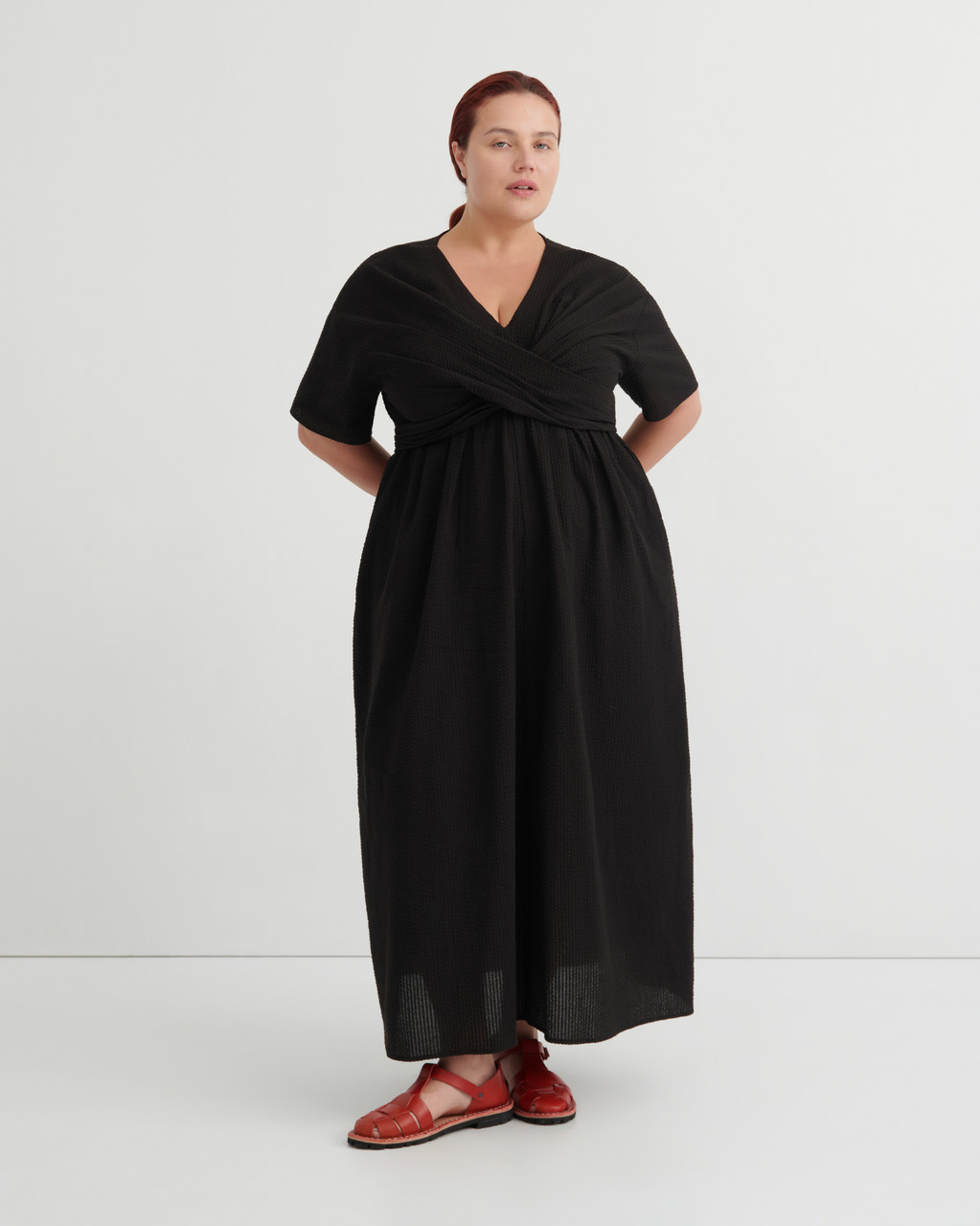A women wears a black v-neck dress and red sandals.