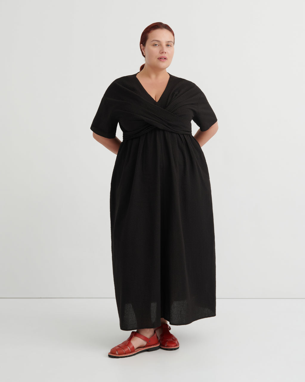 A women wears a black v-neck dress and red sandals.