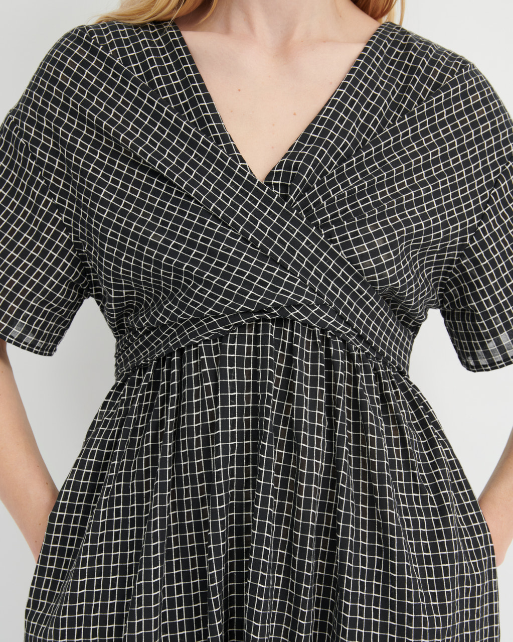 A close-up of a woman wearing a black and white grid-patterned wrap dress with short sleeves and a V-neckline.