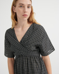 A woman wearing a black and white grid-patterned wrap dress with short flutter sleeves and a V-neckline, photographed against a clean white studio background.
