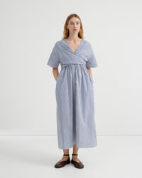 A woman modeling a blue and white vertically striped midi dress with short sleeves, a V-neckline, and a gathered waist, set against a plain white studio background.