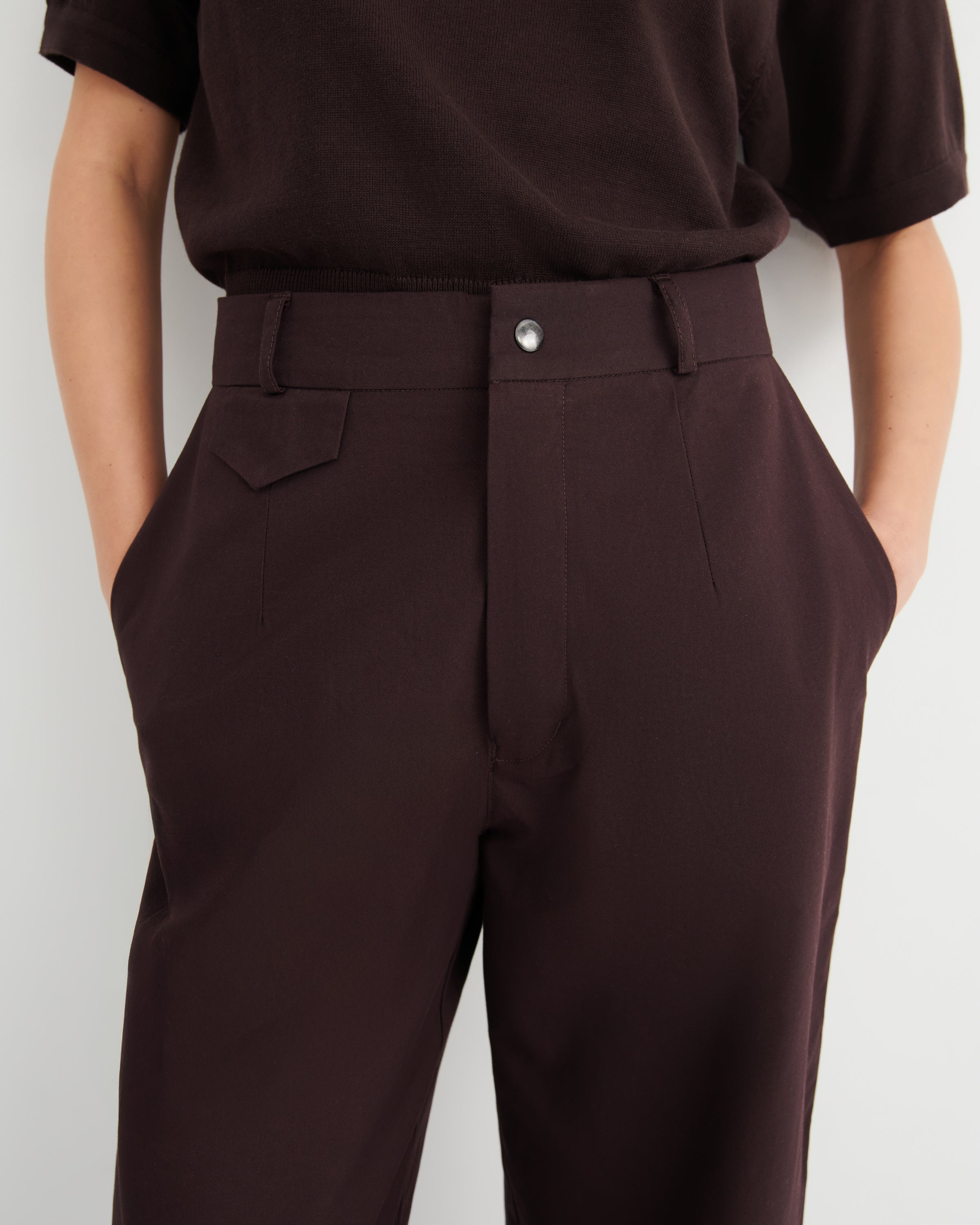 A close-up of a person wearing dark brown tailored trousers and a dark brown short-sleeve top.