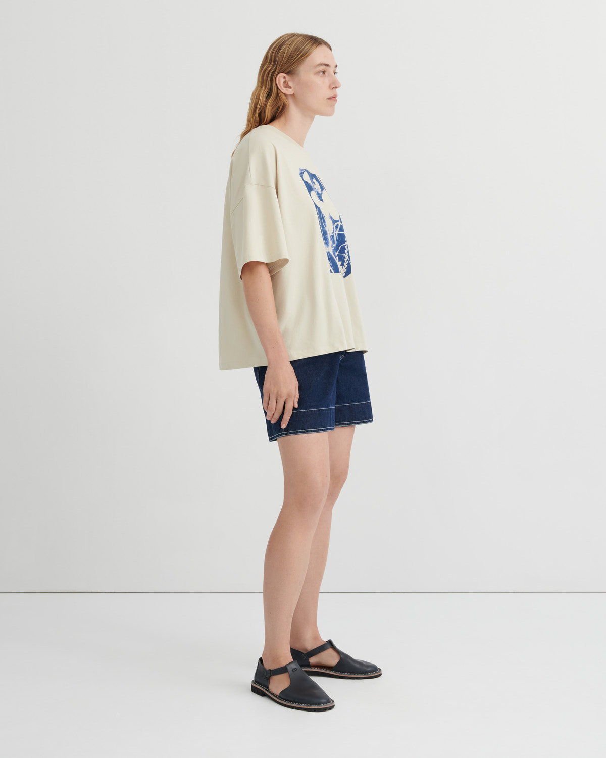 Woman wearing a beige t-shirt with a graphic design and denim shorts on a white background