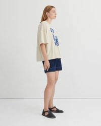 Woman wearing a beige t-shirt with a graphic design and denim shorts on a white background